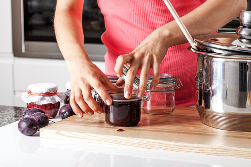 Woman closing the jars with plum jam