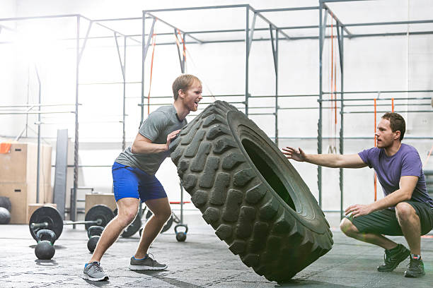 Man assisting at dedicated friend in flipping tire at gym gym