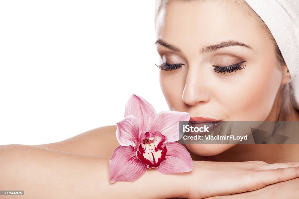 Pure Beauty young beautiful woman with a towel on her head enjoying the scent of orchids Facial Mask - Beauty Product Stock Photo