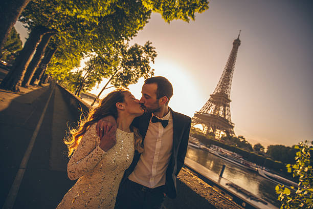 Married couple kissing by the river Photo of young married couple by the river while sun is rising. There is an Eiffel tower in the background. paris france eiffel tower love kissing stock pictures, royalty-free photos & images