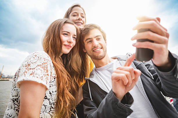 Friends taking a selfie  in Hamburg. Three friends, two girls and a boy, enjoy with a selfie by the Elbe river in Hamburg, taking a self portrait. 