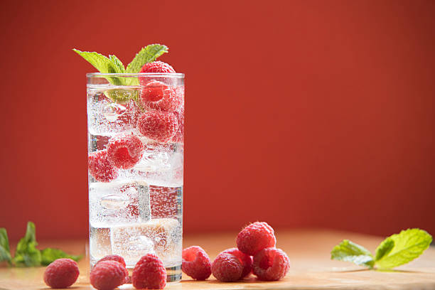 Sparkling Water with Raspberries and Mint A glass of sparkling water with raspberries and mint with a  red background carbonated water photos stock pictures, royalty-free photos & images