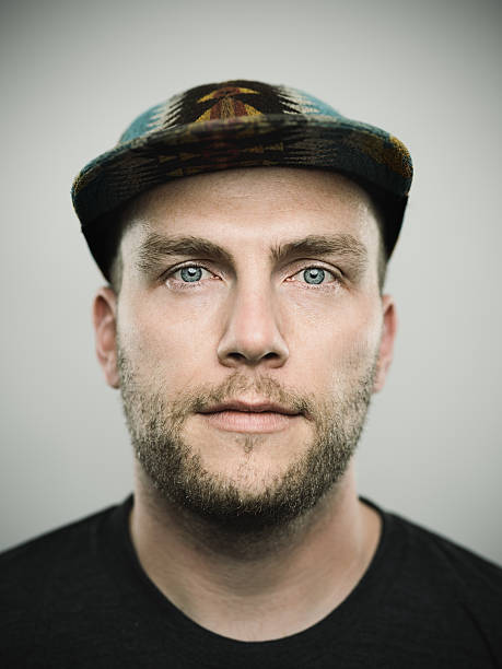 Portrait of a young american man looking at camera Studio portrait of a caucasian american young man looking at camera with relaxed expression. The man has around 35 years and has short hair and casual clothes, wearing a baseball cap. Vertical color image from a medium format digital camera. Sharp focus on eyes. istockalypse stock pictures, royalty-free photos & images