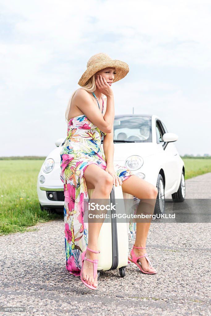 Female Road Trip Full length of irritated woman sitting on luggage by broken down car 20-29 Years Stock Photo