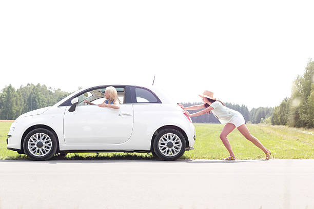 Female Road Trip Woman pushing broken down car on country road vehicle breakdown stock pictures, royalty-free photos & images