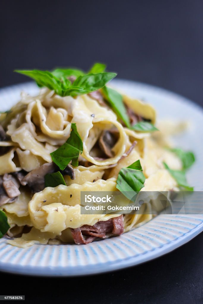 Pappardelle with mushroom, bacon, parmesan and basil Plate of pappardelle pasta with mushroom, bacon, parmesan cheese and fresh basil leaves on black background. 2015 Stock Photo