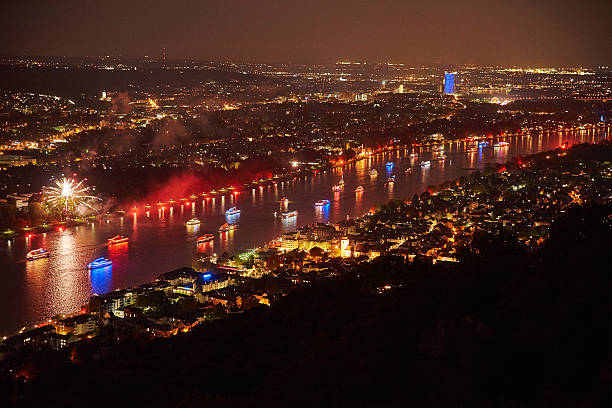Luminous ships sail on the river. In the background is an illuminated skyline.