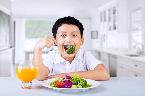 rapaz comendo brócolis em casa - dieting juice carrot tomato - fotografias e filmes do acervo