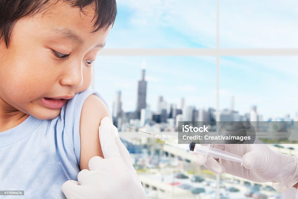 Boy patient scared of vaccine syringe A boy is scared looking at his arm because he's going to be vaccinated by the doctor Child Stock Photo