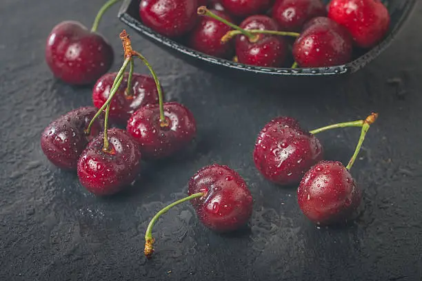 Sweet cherry fruit with water drops on black stone background
