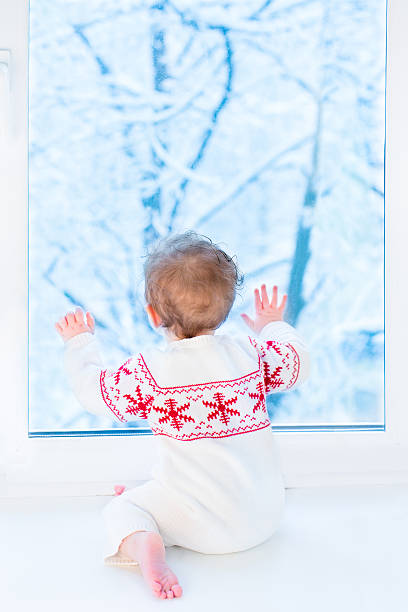 istock Little baby sitting at window watching snow covered trees 477604101