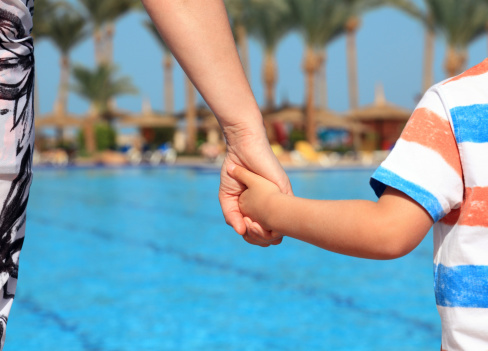 Mother and son holding hands on vacation looking at swimming pool concept for family vacations, child safety and single parent holiday