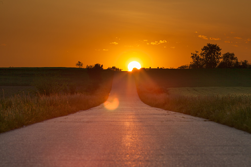 Driving on an empty open asphalt road towards the setting sun.