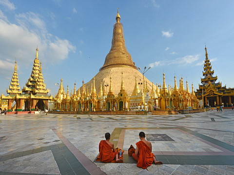 Yangon, Myanmar - December 4th 2014:Two monks sit in front of the golden stupa of Shwedagon Pagoda, the most famous sight of Burma