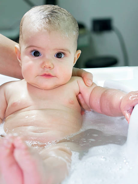 istock baby girl smiles during bathing supported by mom 477621033