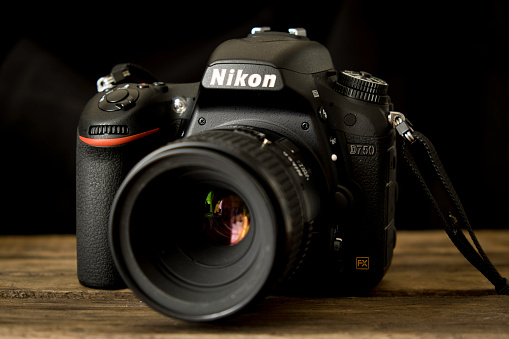 Annapolis, USA - January 15, 2015: A Nikon D750 digital single lens reflex camera with the Nikon 60mm macro lens attached on a wooden surface with black background.