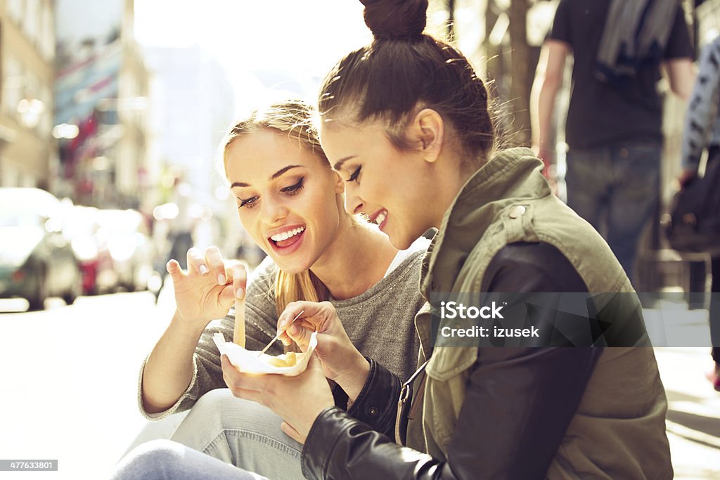 Young women in the city Two young women sitting on the city street and eating take away chips. Eating Stock Photo