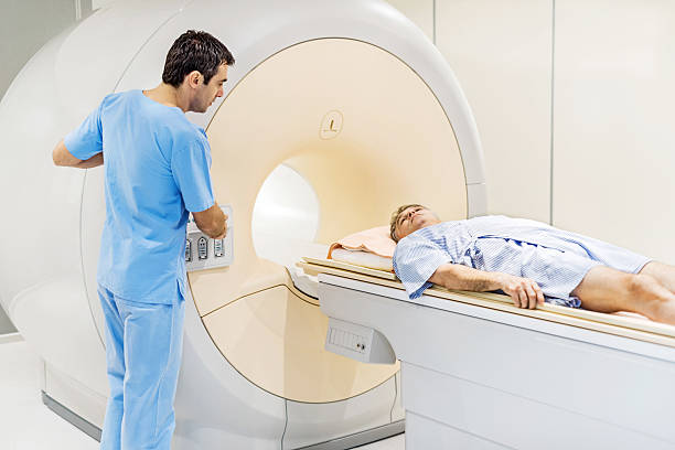 Mature man receiving an MRI Scan. Mature man entering into the MRI Scanner, while radiologist is pressing the start button.   pet scan photos stock pictures, royalty-free photos & images