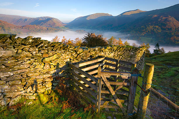 English Lake District: Grasmere sunrise A wooden gate on the hills above Grasmere, in the English Lake District, is lit by the rising sun, with the Cumbrian mountains in the distance and the misty lake visible in the valley below. grasmere stock pictures, royalty-free photos & images