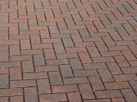 Photo showing a brick paved driveway, with interconnecting bricks laid upon a base of compacted hardcore and sand, forming a herringbone pattern.