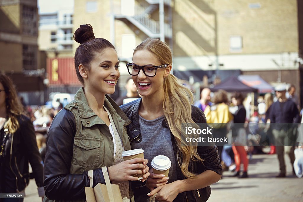 Friends laughing outdoors Two young women standing on the city street, holding take coffee in hands and having fun. Friendship Stock Photo