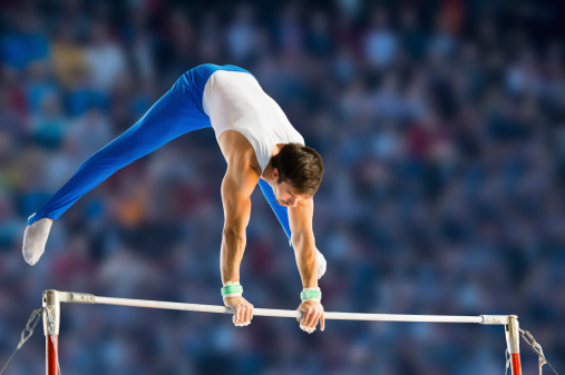 Side view of young man performing short routine on horizontal bar, artistic gymnastics