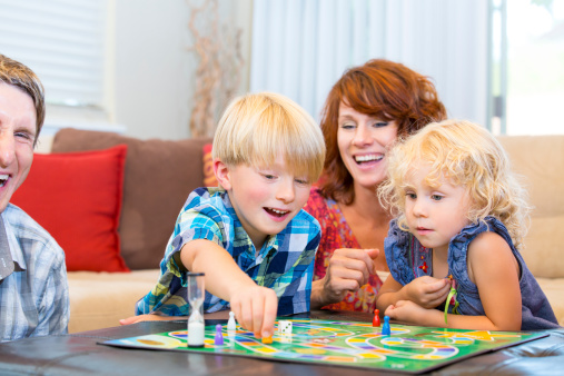 Family with two little kids having fun playing board games.  Note: The game is one-of-a-kind and created specifically for stock use. You might also be interested in these: