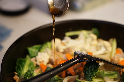Cooking and pouring sauce into Asian stir fry.