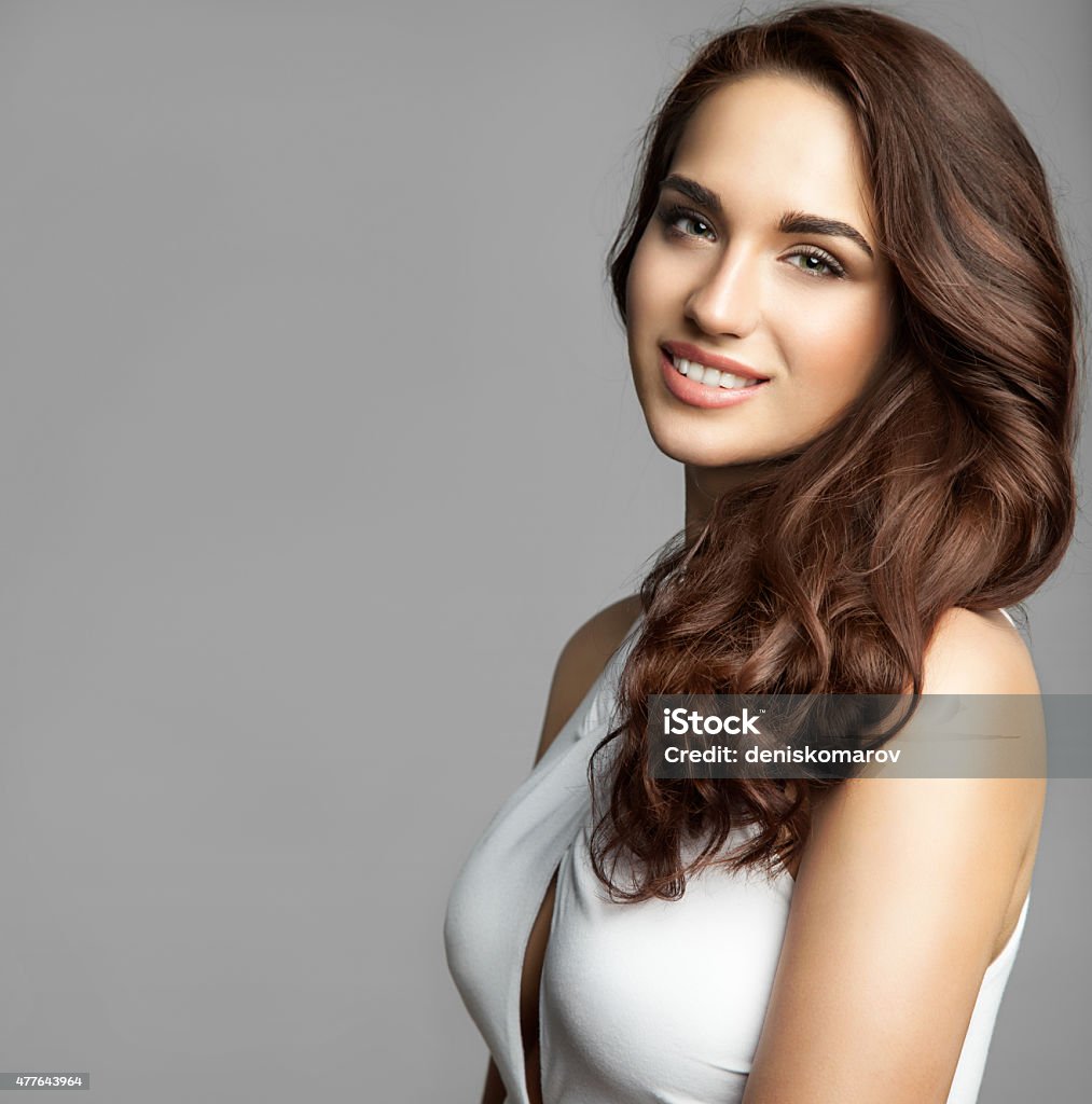 woman with a long thick curly hair Portrait of a woman in a white dress with a long thick curly hair on gray background isolated Beautiful Woman Stock Photo