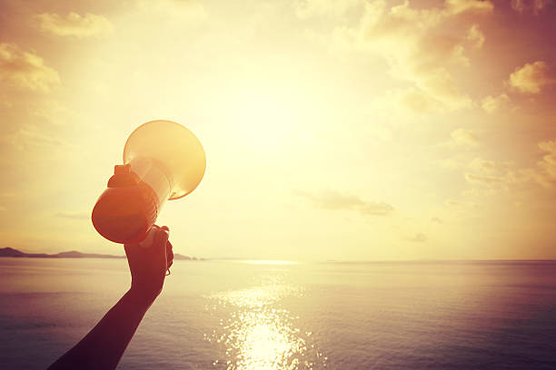 istock hands hold megaphone with sea under blue sky background 477648618