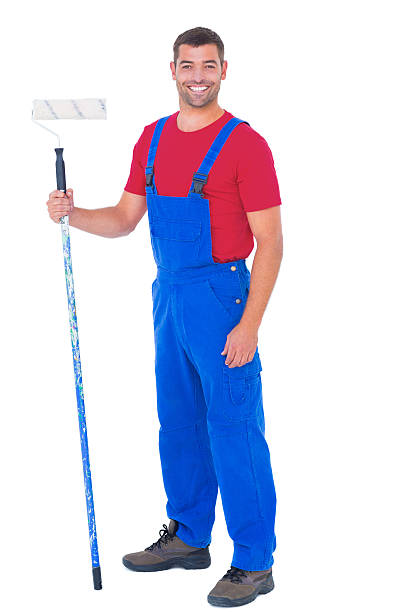 istock Handyman in overalls holding paint roller on white background 477659302