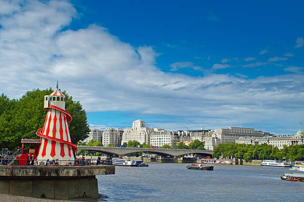 London, United Kingdom - September 7, 2013: A view of the River Thames and its banks looking North West from the South Bank.  In the foreground is a red and white 'Helter Skelter' and in the background is the North Bank near Embankment.  Some tourists and day trippers are at the base of the 'Helter Skelter'.