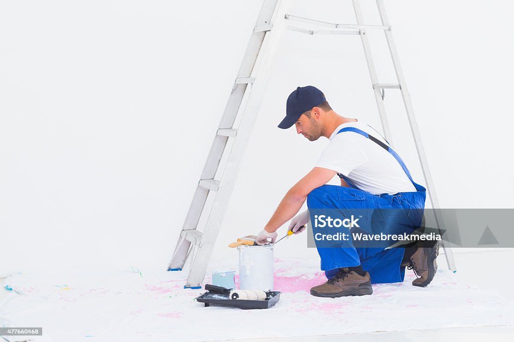 Side view of handyman in overalls opening paint can Full length side view of handyman in overalls opening paint can at home Opening Stock Photo