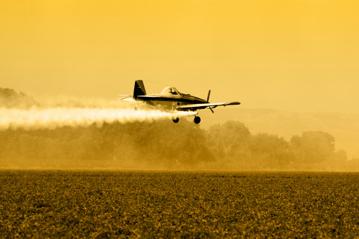 Crop duster, aircraft silhouette over tilled agricultural field.