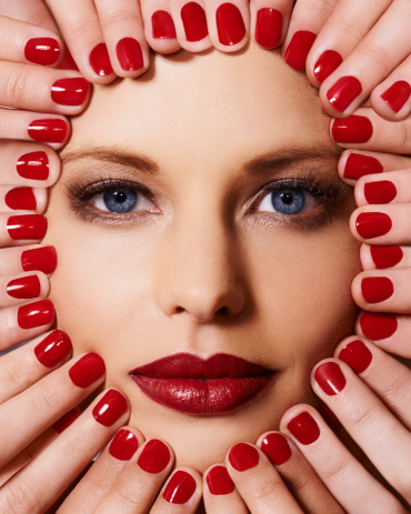 Cropped image of a woman wearing red lipstick looking at the camera with fingers with red polish touching her face