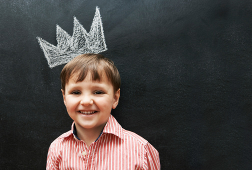 Studio shot of an adorable young boy with a drawing of a crown on a blackboard behind him