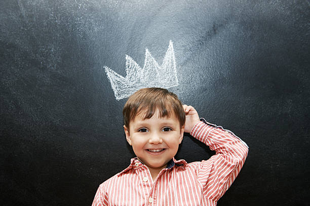 Preschool royalty Studio shot of an adorable little boy with a drawing of a crown on a blackboard behind him crown headwear photos stock pictures, royalty-free photos & images