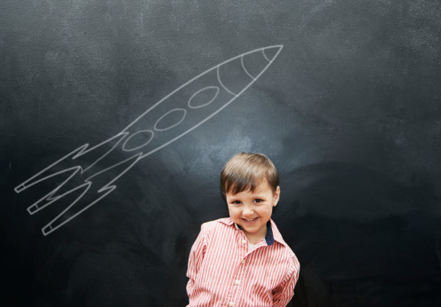 Studio shot of an adorable little boy with a chalk drawing of a rocket behind him