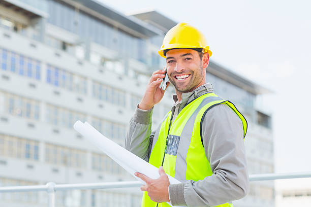 istock Smiling male architect with blueprints talking on mobile phone 477669354