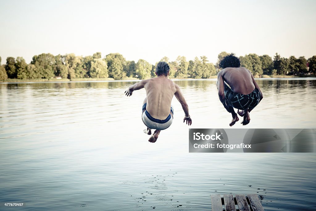 carefree summer day: teenagers jumping into a lake young adults jump an ass-bomb into a lake Adolescence Stock Photo