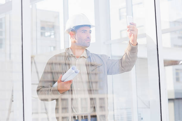 istock Architect with blueprints photographing through mobile phone in office 477672582