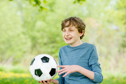 A little boy with down syndrome holds a soccer ball as he plays outside at a park on a beautiful sunny day.