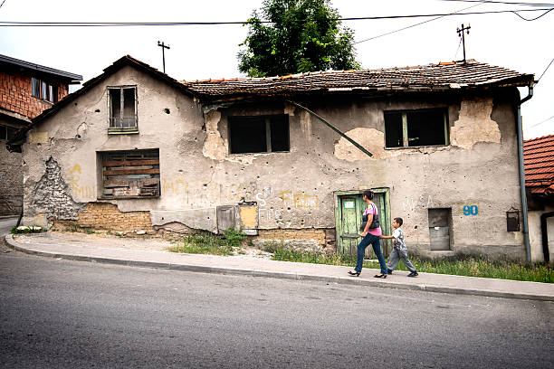 Sarajevo, Bosnia and Herzegovina - August 15, 2014: Scars of war in Sarajevo are still visible. Here a Mother and his boy are walking in a bombed road