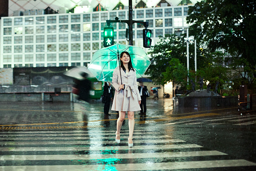 Smiling Japanese woman with an umbrella crossing a street in the rain in Shibuya, Tokyo. Shot from Istocklypse Tokyo 2015.