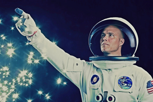 This is a portrait of an astronaut pointing. The background is a pure black allowing for endless copy above. The Saturn and Earth patches are fake and were created in Photoshop.