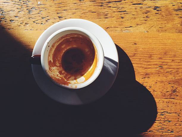 Just-finished espresso in white cup, saucer on sunny wooden table