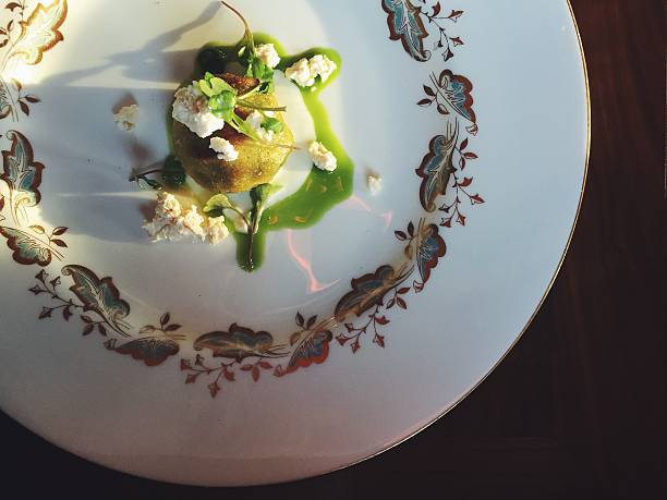 A vegetarian appetizer consisting of a single ricotta gnudo (gnudi) topped with crumbled fresh ricotta cheese, a bright green puree made with nettles and a few microgreens, on top of a vintage white plate with a leaf design around it. Sunlight coming in from the left.