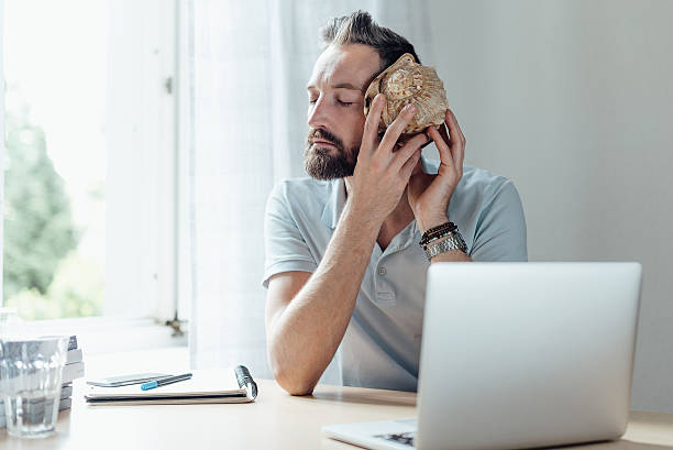 man listening to shell at ear at the office