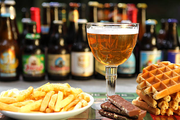This is an image of all the food and drinks that Belgium is famous for: Belgian beer, Belgian waffles, Belgian chocolate, and traditional fries with mayonnaise. A variety of Belgian beer bottles are out of focus in the background.