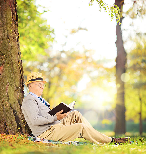 istock Senior man sitting on grass and reading a book 477703317
